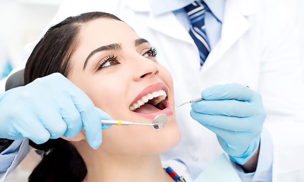 Woman smiling while a dentist checks her teeth with tools