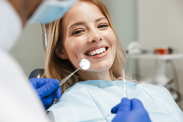 Woman smiling while a dentist checks her teeth with tools